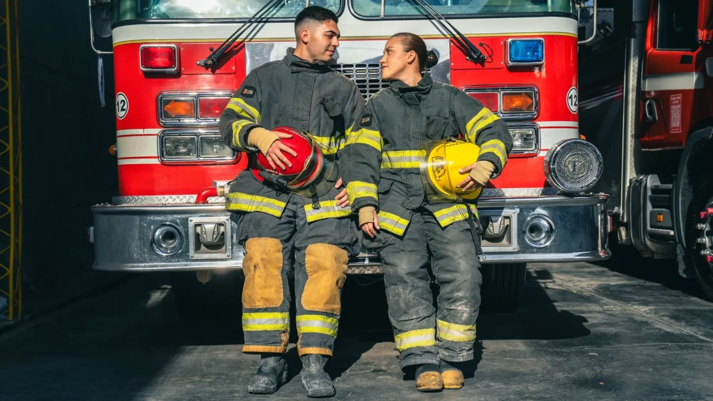 Bombeiros sentados no estribo de uma viatura vermelha