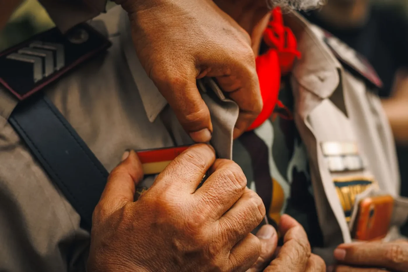 Mãos prendendo uma medalha na farda de um militar veterano