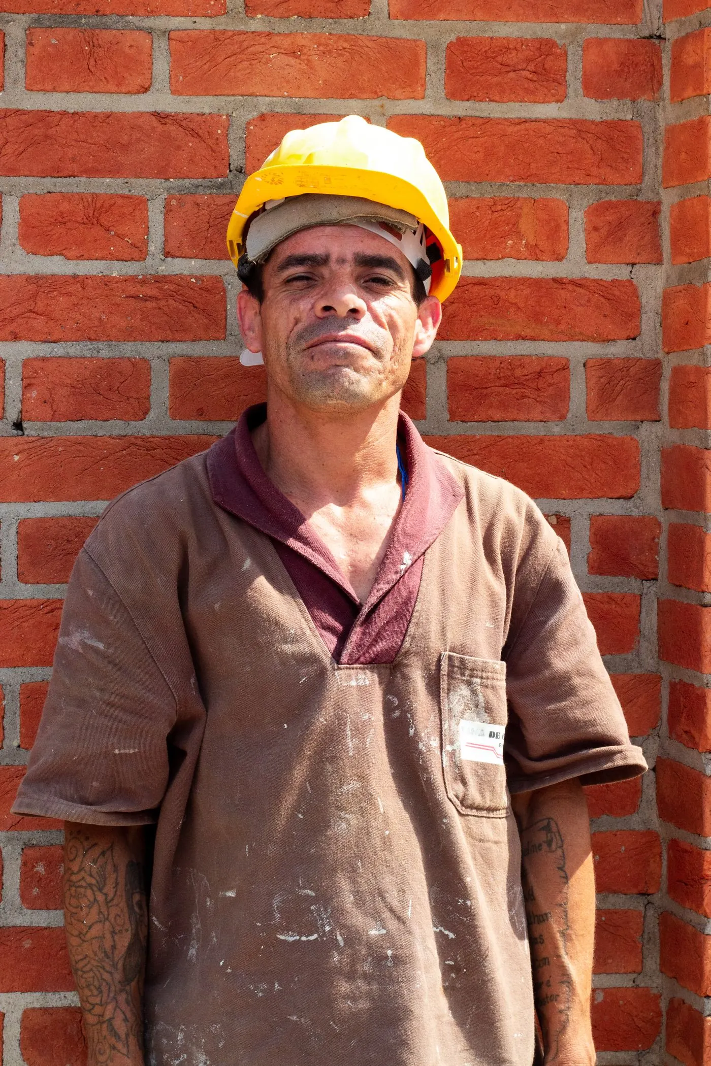Trabalhador de capacete amarelo diante de uma parede de tijolos